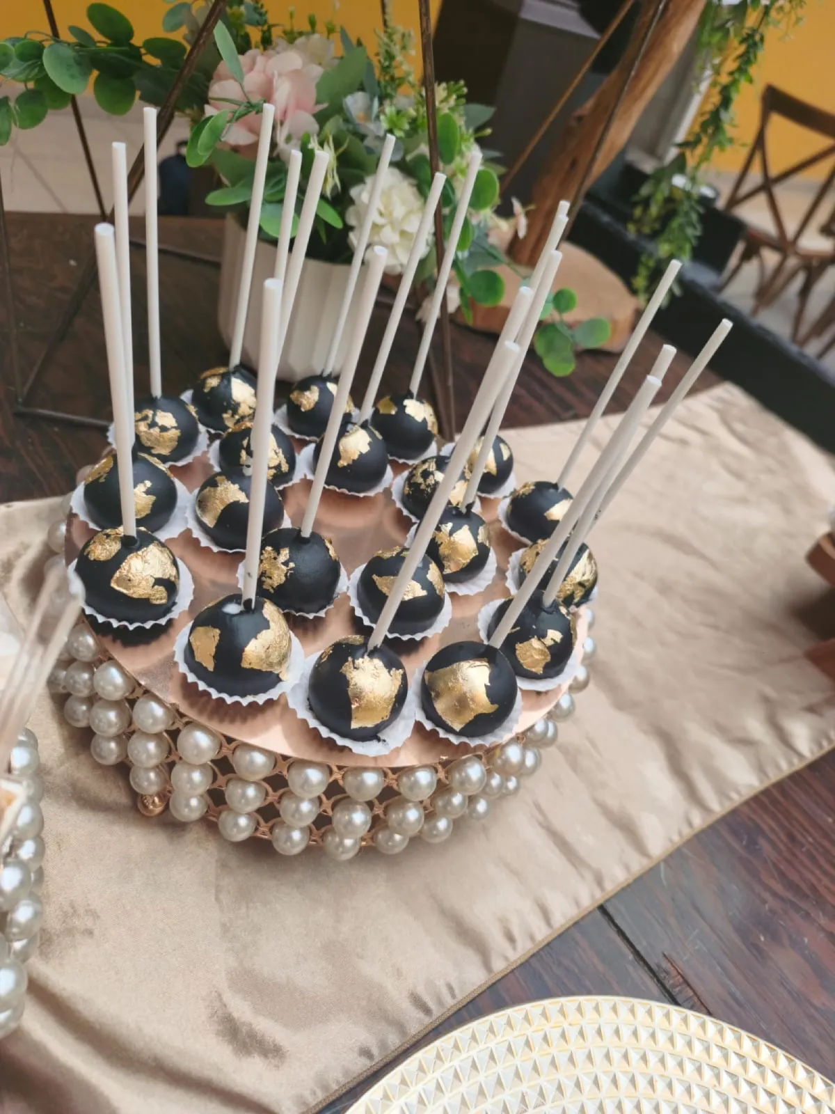 Cakepops negros con hoja de oro sobre base de perlas, en la mesa de postres