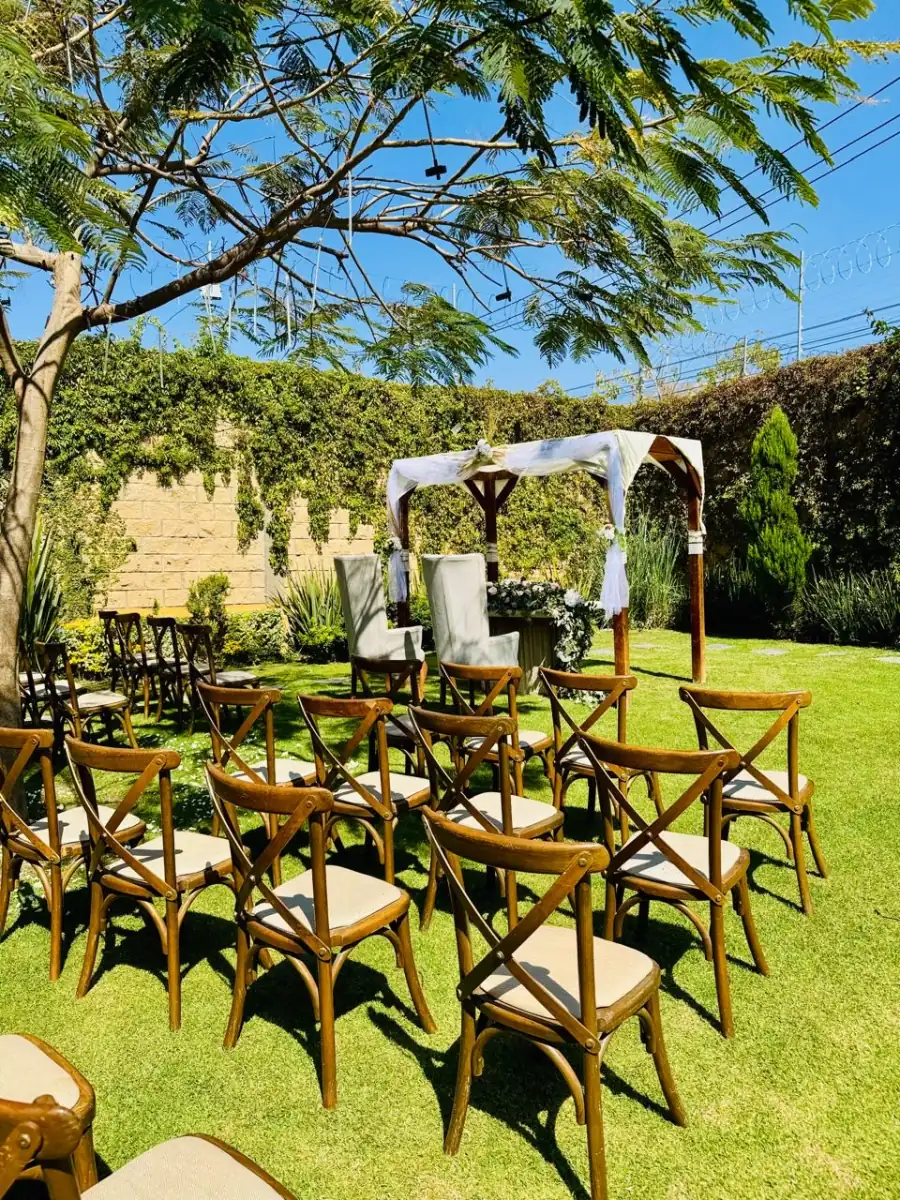 Pérgola con telas blancas y sillas de madera bajo el cielo azul en el jardín de Bonanza