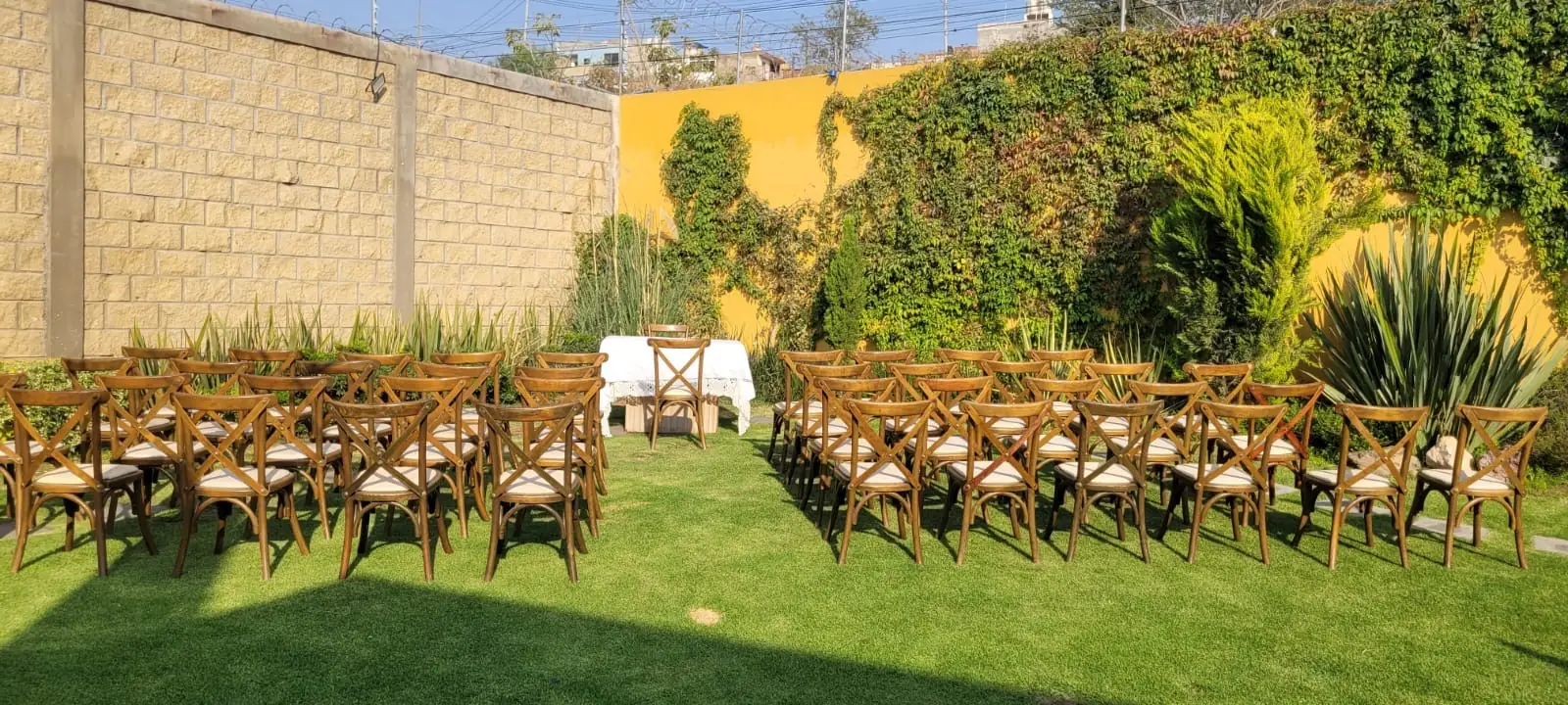 Jardín de Bonanza en la tarde: sillas de madera en dos bloques y mesa de ceremonia frente al muro de enredadera